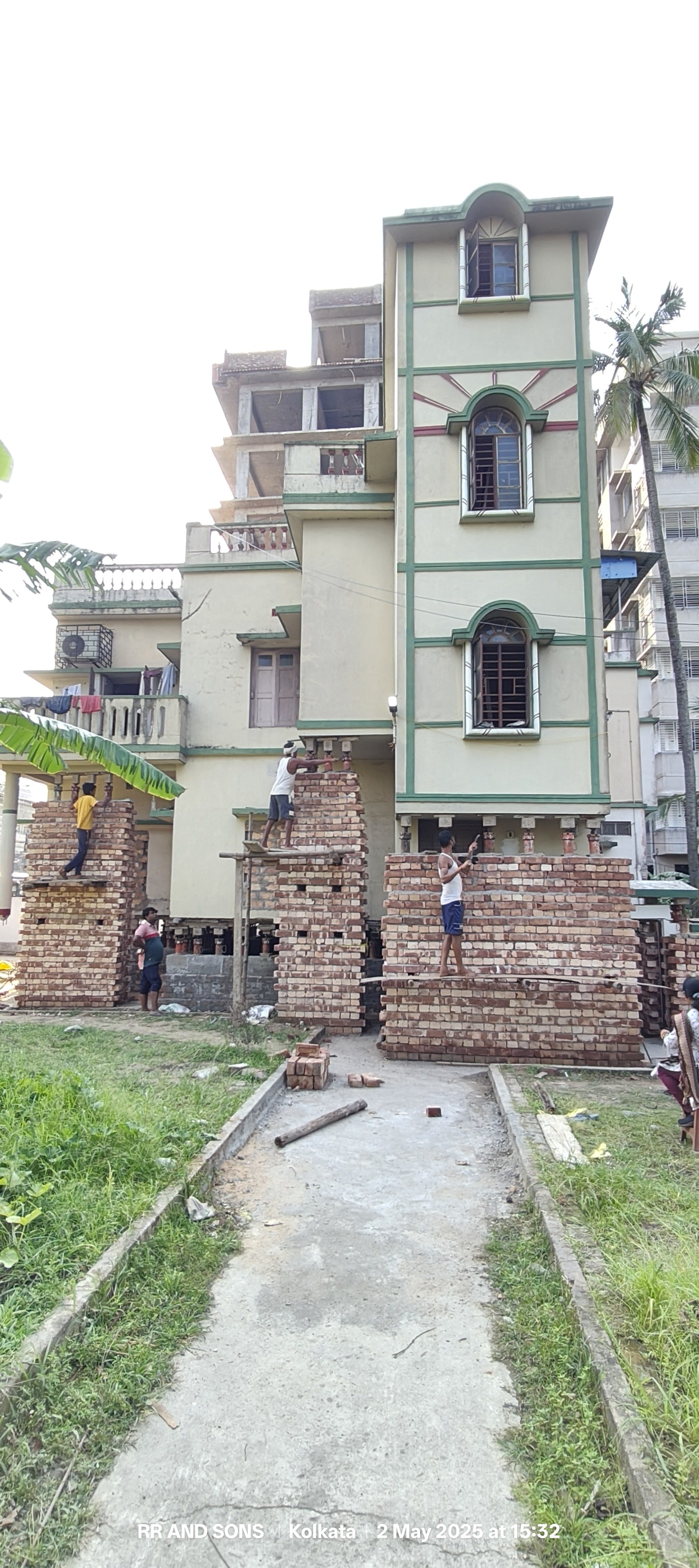 Engineers and masonry crew constructing brick piers under lifted building in Kolkata, West Bengal
